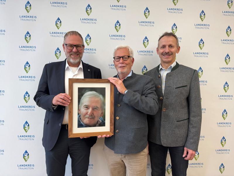 Bildunterschrift:  Landrat Andreas Danzer (li.) bedankt sich gemeinsam mit Florian Seestaller, Leiter der Bürgerhilfsstelle im Landratsamt Traunstein (re.), bei Peter Schimpf, Vorstand der Georg Johannes Hipp-Stiftung (Mi.), für die großzügige Spende in Höhe von 20.000 Euro. Das Foto zeigt die drei bei der Spendenübergabe im Landratsamt Traunstein – mit einem Porträt des Stifters Georg Johannes Hipp, dessen Engagement für Menschen in Not fortgeführt wird.  ©Landratsamt Traunstein
